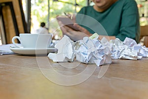 Wwoman hand using cell phone working after hours with crumpled paper on table.