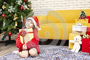 X-mas and holiday concept. Happy childen girl with gift box. Girl in christmas cap hands present wrapped with gold paper and red