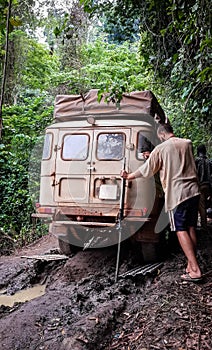 4x4 offroad vehicle stuck on muddy dirt road with young man trying to recover it in rain forest of Cameroon, Africa