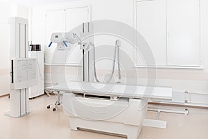 X-ray department in modern hospital. Radiology room with scan machine with empty bed. Technician adjusting an x-ray