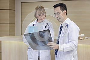 X-ray prints are examined by hospital staff. While looking at an x-ray image, two male medics confer. Two Caucasian doctors