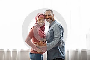 We'll Be Parents. Happy Pregnant Islamic Spouses Posing Near Window At Home