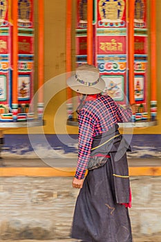 XIAHE, CHINA - AUGUST 25, 2018: Devotee passes a row of praying wheels around Labrang Monastery in Xiahe town, Gansu