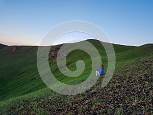 Xilinhot - A man sitting on a stone on a green hill in Xilinhot, Inner Mongolia and enjoys a sunset. He is wearing a cowboy hat