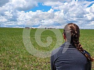 Xilinhot - A woman with braided hair watching a heard of horses grazing under wind turbines build on a vast pasture