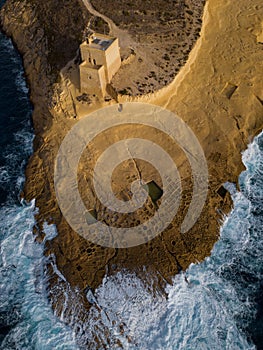 Xlendi Tower with rough waves aerial top down view at golden hour Gozo Malta