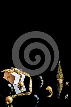 Xmas background gold. White gift box with golden ribbon, New Year balls and winter tree in Christmas composition on black