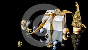 Xmas background gold. White gift box with golden ribbon, New Year balls and winter tree in Christmas composition on black