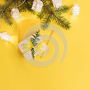Xmas business greeting card. Yellow notepad on 2021, fir branches, Xmas lights white lodges, gift box on yellow.