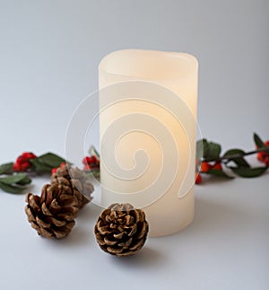 White christmas candle and christmas decoration on white background. Pine cones and red berries branch ornaments.