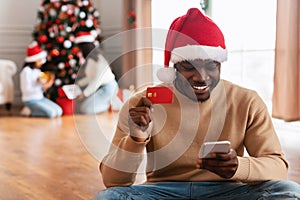 Xmas Online Shopping. Black man using cellphone showing credit card