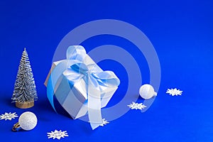 Xmas sale. White gift box with blue ribbon, winter tree, Snowflakes and Silver balls in Christmas composition on blue background