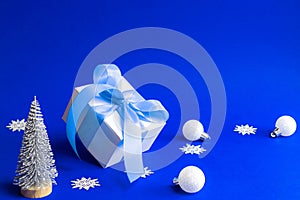 Xmas wreath. White gift box with blue ribbon, winter tree, Snowflakes and Silver balls in Christmas composition on blue background