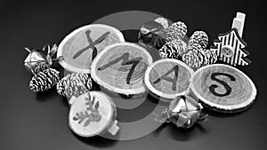 XMAS written on wooden disks with pine cones and Christmas ornaments, dark background