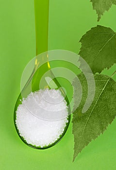 Xylitol birch sugar on plastic spoon over green