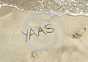 YAAAS Gen Z Millennial Slang Written on a Sandy Beach With Ocean Wave and Footprints