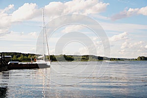 Yacht on blue peaceful lake on green forest and blue sky background