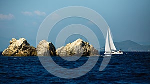 Yacht boat with white sails near the rocks in the Aegean sea. Travel.