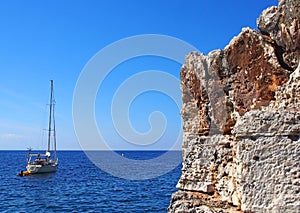 Yacht on a bright calm Mediterranean sea next to beautiful rugged cliffs on the minorcan coastline in bright blue summer sunshin