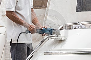 Yacht maintenance. A man polishing side of the white boat in the