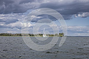 Yacht sailboat sailing alone on blue sea waters on a beautiful sunny day with blue sky and white clouds.