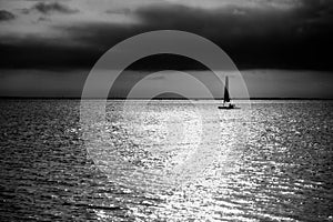 The yacht sailing on the waves of the sea bay in the rays of the evening setting sun against the backdrop of a stormy sky