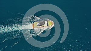 Yacht with sun loungers at the stern floating on the water surface in summer, aerial top view