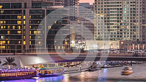 Yachts and boats with tourists staying near shoping mall and passing under a bridge in Dubai Marina district day to