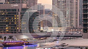 Yachts and boats with tourists staying near shoping mall and passing under a bridge in Dubai Marina district day to