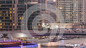 Yachts and boats with tourists staying near shoping mall and passing under a bridge in Dubai Marina district day to