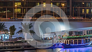 Yachts and boats with tourists staying near shoping mall and passing under a bridge in Dubai Marina district night