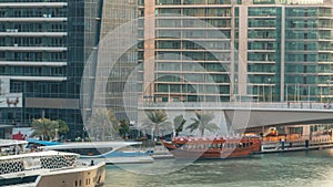 Yachts and boats with tourists staying near shoping mall and passing under a bridge in Dubai Marina district timelapse.