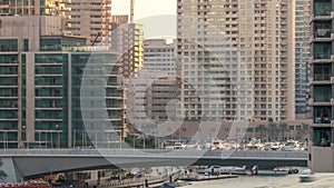 Yachts and boats with tourists staying near shoping mall and passing under a bridge in Dubai Marina district timelapse.