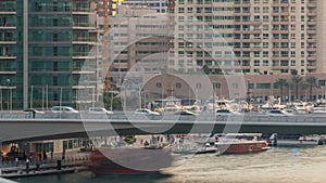 Yachts and boats with tourists staying near shoping mall and passing under a bridge in Dubai Marina district timelapse.