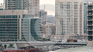 Yachts and boats with tourists staying near shopping mall and passing under a bridge in Dubai Marina district day to