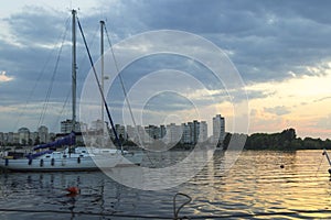 Yachts with high masts and lowered sails on the background of urban buildings. Sunset