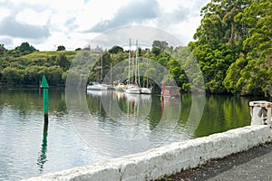 Yachts and houseboat moored behind red and green channel marker in bay surrounded by green trees