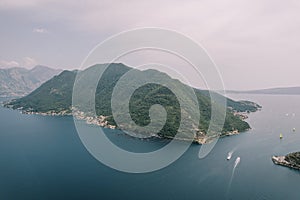 Yachts sail along the Bay of Kotor past the green mountain range. Aerial view
