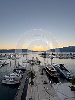 Yachts stand at the pier with palm trees in the bay against the backdrop of sunset over the mountains