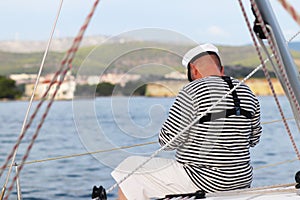 Yachtsman in marine clothing looking into the distance sitting on board a sailing yacht. Sea fishing from the ship. Peaceful state