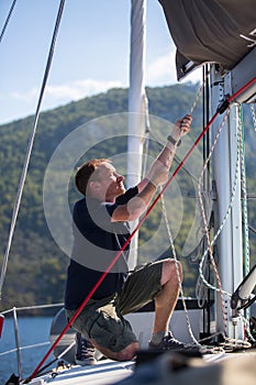 Yachtsman pulls the rope on the mast, on his sailing yaht boat