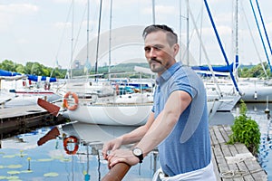 Yachtsman standing near of pier barrier with boats. Bearded man looking to far before journey near of yacht.