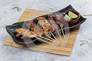 Yakitori Japanese-Style Grilled Chicken Skewers with chicken and internal organ served with sliced lime on black stone plate.