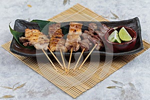 Yakitori Japanese-Style Grilled Chicken Skewers with chicken and internal organ served with sliced lime on black stone plate.
