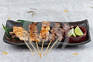 Yakitori Japanese-Style Grilled Chicken Skewers with chicken and internal organ served with sliced lime on black stone.