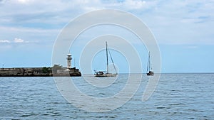 Yalta lighthouse, two yachts go out to the calm sea.
