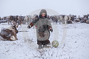 The Yamal Peninsula. Reindeer with a young reindeer herder. Happy boy on reindeer herder pasture playing with a ball in winter