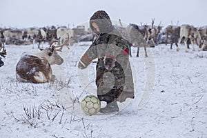 The Yamal Peninsula. Reindeer with a young reindeer herder. Happy boy on reindeer herder pasture playing with a ball in winter