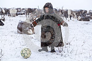 The Yamal Peninsula. Reindeer with a young reindeer herder. Happy boy on reindeer herder pasture playing with a ball in winter