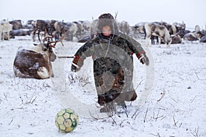 The Yamal Peninsula. Reindeer with a young reindeer herder. Happy boy on reindeer herder pasture playing with a ball in winter